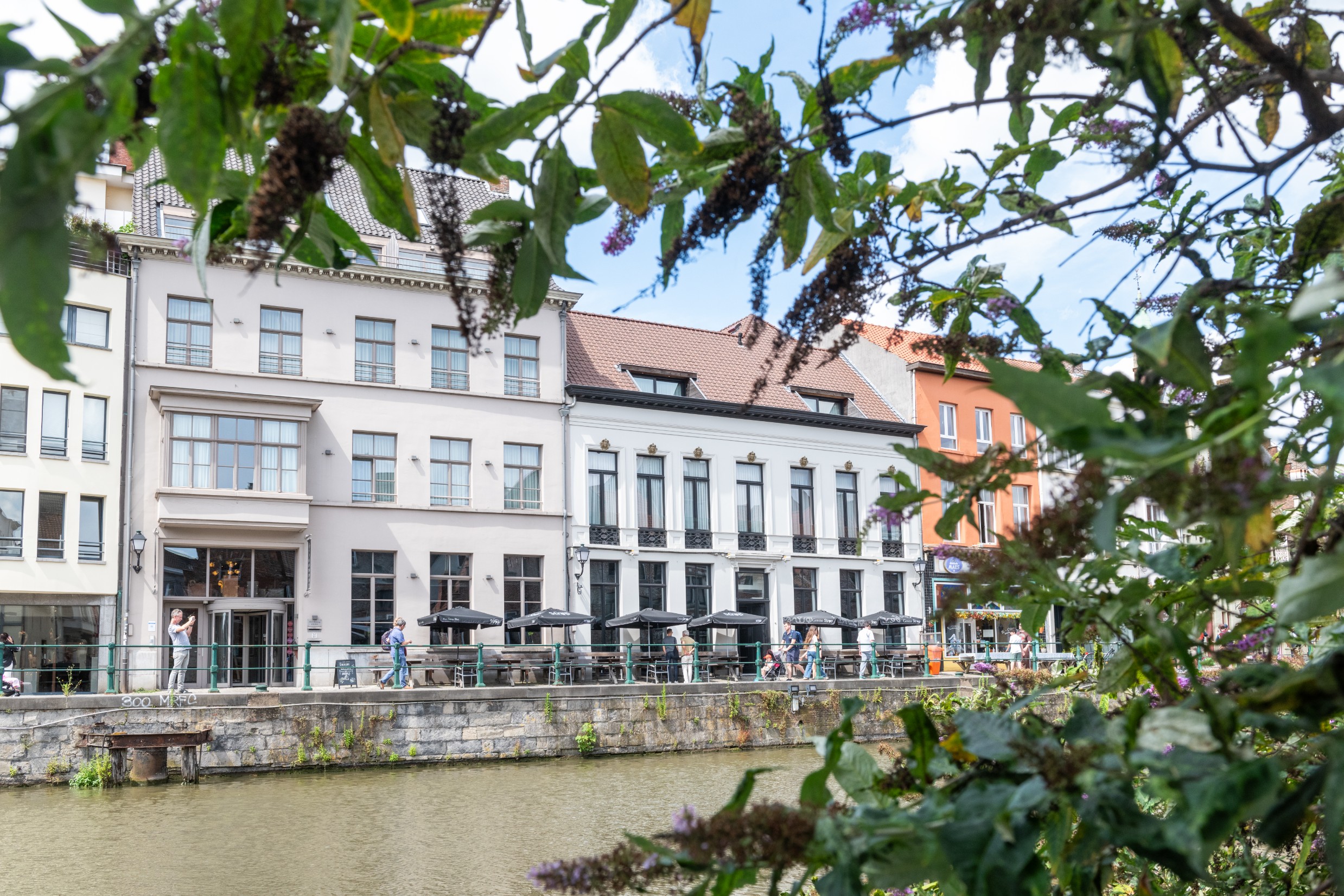 Terras van Hotel Harmony aan de Leie, met bloeiende klimplanten en zicht op historische gevels
